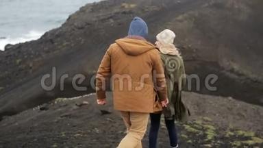在刮风的日子里，年轻夫妇在海边的悬崖上散步，牵手在大自然上浪漫的约会。